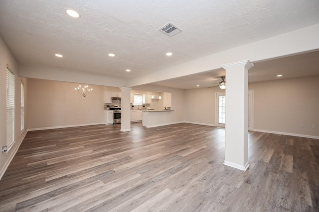 unfurnished living room featuring decorative columns, visible vents, wood finished floors, and ceiling fan with notable chandelier