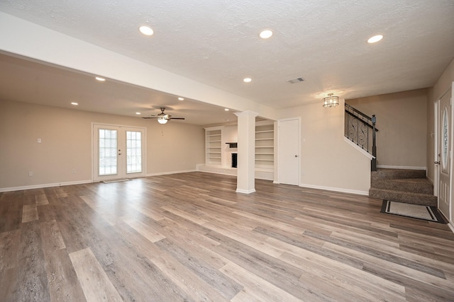 unfurnished living room with stairs, baseboards, a textured ceiling, and wood finished floors