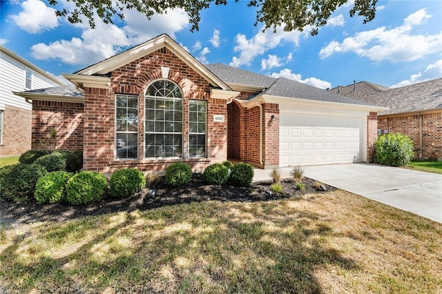 ranch-style home with brick siding, a shingled roof, concrete driveway, an attached garage, and a front yard