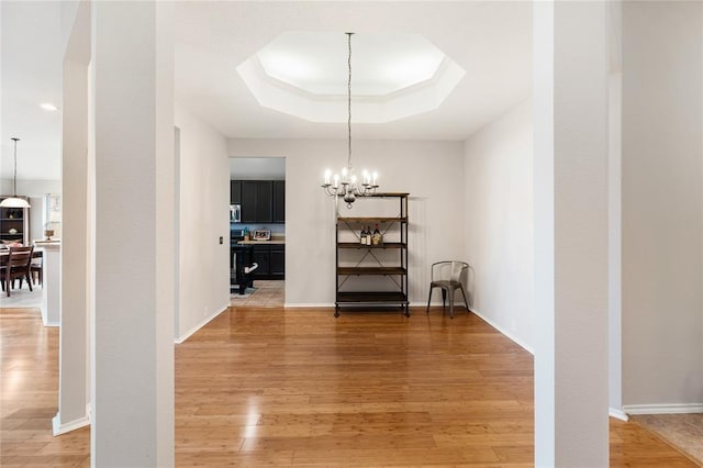 unfurnished dining area featuring a raised ceiling, baseboards, light wood finished floors, and an inviting chandelier