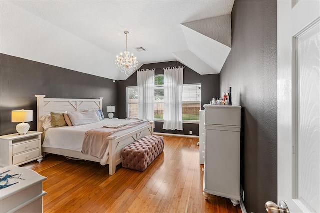 bedroom featuring light wood finished floors, visible vents, vaulted ceiling, and a chandelier