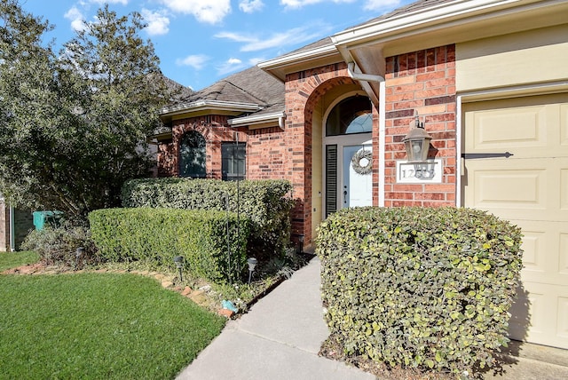 view of exterior entry with a garage, brick siding, and roof with shingles