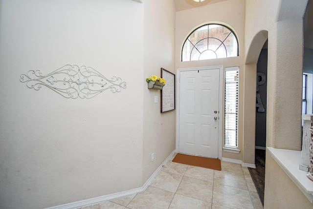 foyer featuring light tile patterned floors, a towering ceiling, and baseboards