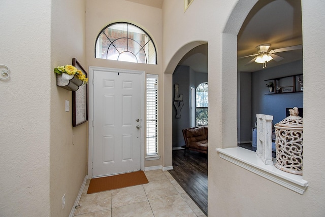 foyer featuring arched walkways, ceiling fan, light tile patterned floors, and baseboards