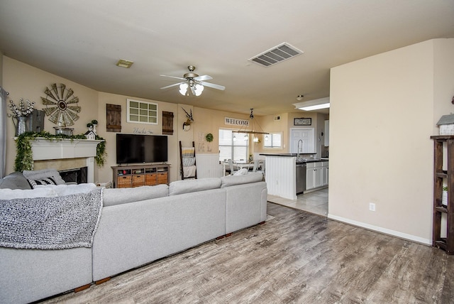 living area with ceiling fan, light wood-style flooring, a fireplace, and visible vents