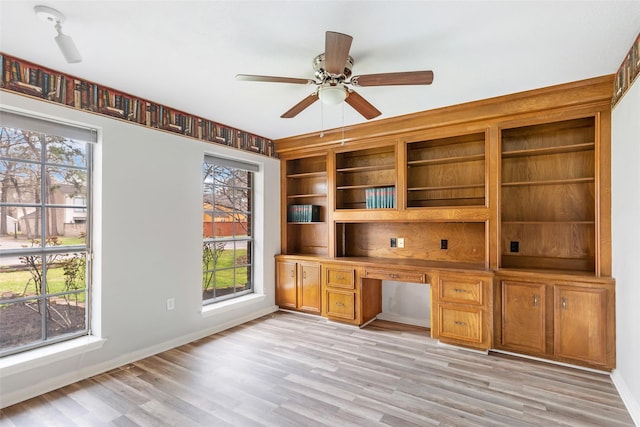 unfurnished office with a ceiling fan, built in study area, light wood-style flooring, and baseboards