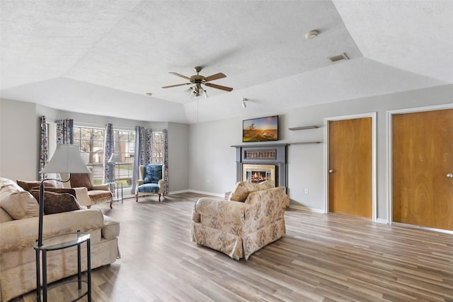 living room with wood finished floors, visible vents, baseboards, a tray ceiling, and a glass covered fireplace