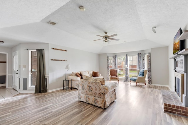 living room featuring ceiling fan, a fireplace, a raised ceiling, and light wood-style flooring