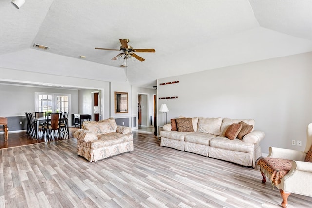 living area featuring baseboards, visible vents, a ceiling fan, vaulted ceiling, and light wood-type flooring