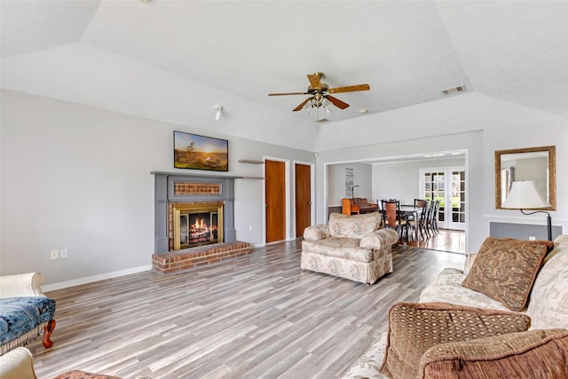 living area featuring a fireplace, wood finished floors, visible vents, baseboards, and vaulted ceiling