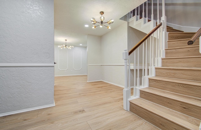 staircase featuring a textured wall, a notable chandelier, baseboards, and wood finished floors