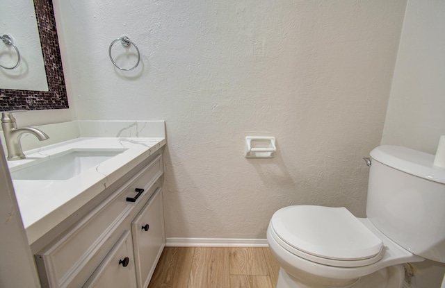 half bathroom with a textured wall, toilet, vanity, wood finished floors, and baseboards