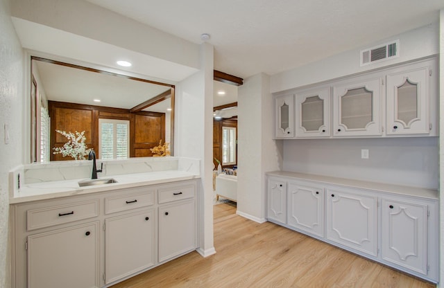 kitchen with a sink, visible vents, light countertops, light wood-type flooring, and glass insert cabinets