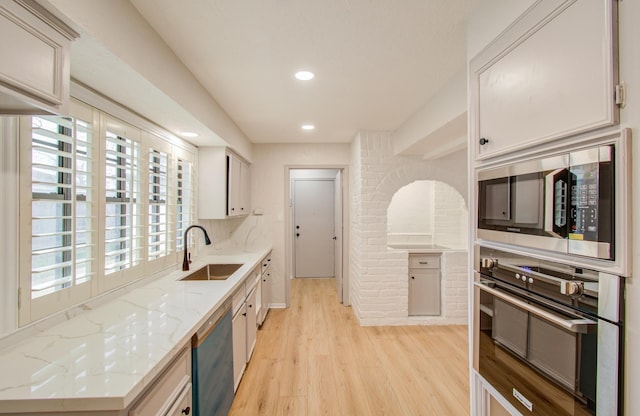 kitchen with dishwashing machine, wall oven, a sink, light wood finished floors, and stainless steel microwave