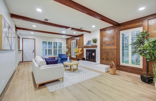 living area featuring recessed lighting, visible vents, light wood-style floors, a brick fireplace, and beamed ceiling