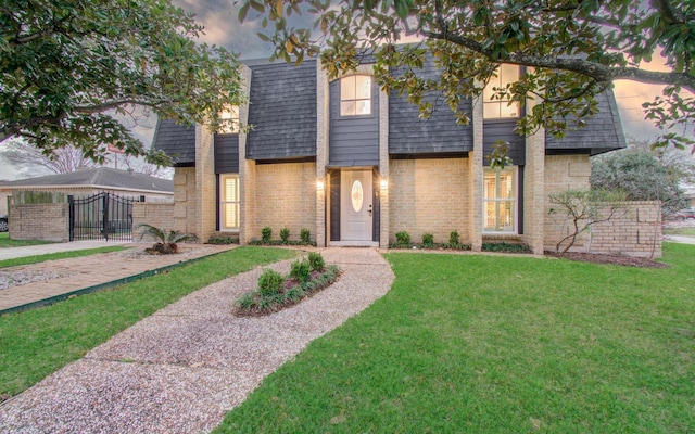 view of front of home with roof with shingles, a yard, brick siding, mansard roof, and a gate