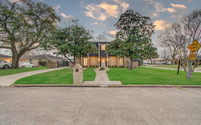 view of front of house with driveway, brick siding, and a lawn