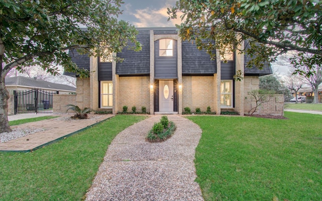 view of front of house with a shingled roof, mansard roof, a gate, a front yard, and brick siding