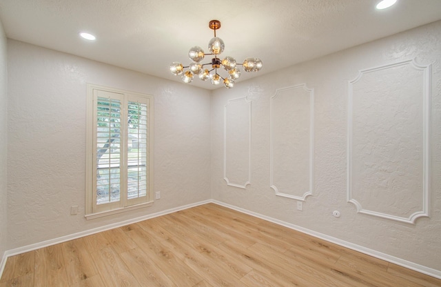 empty room with a textured wall, recessed lighting, a notable chandelier, wood finished floors, and baseboards