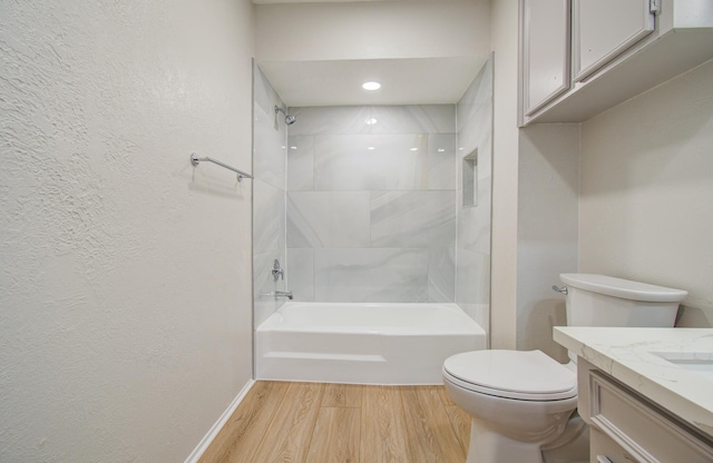 full bathroom with a textured wall, toilet, bathing tub / shower combination, wood finished floors, and vanity