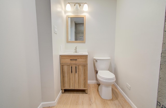 half bath with vanity, wood finished floors, toilet, and baseboards