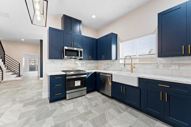 kitchen with blue cabinets, a sink, tasteful backsplash, appliances with stainless steel finishes, and light stone countertops