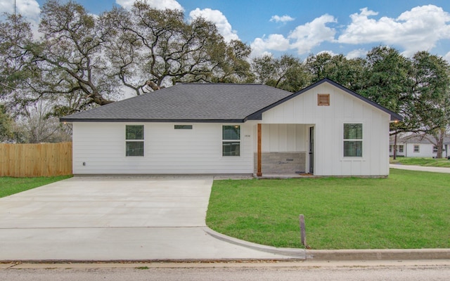 ranch-style house with roof with shingles, a front lawn, board and batten siding, and fence