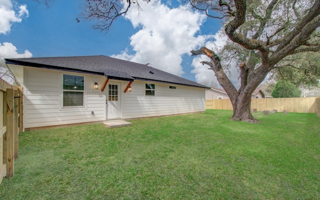 rear view of property with a shingled roof, a lawn, and a fenced backyard