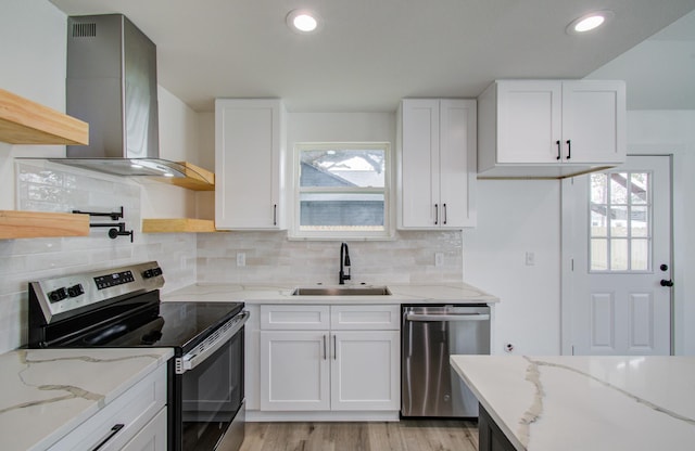 kitchen featuring light stone counters, stainless steel appliances, a sink, white cabinetry, and wall chimney exhaust hood