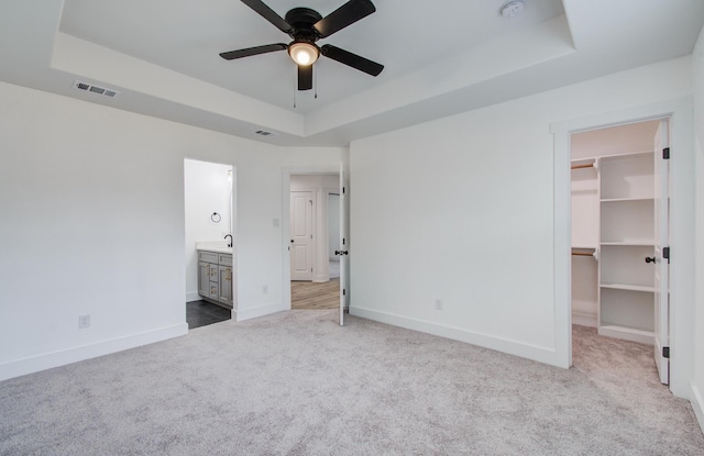 unfurnished bedroom with baseboards, visible vents, a tray ceiling, a walk in closet, and carpet flooring