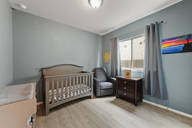 bedroom featuring a crib, baseboards, and wood finished floors