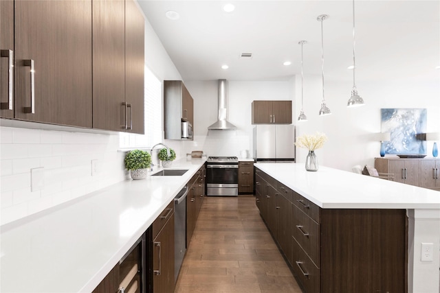 kitchen with light countertops, wall chimney exhaust hood, a kitchen island, appliances with stainless steel finishes, and a sink