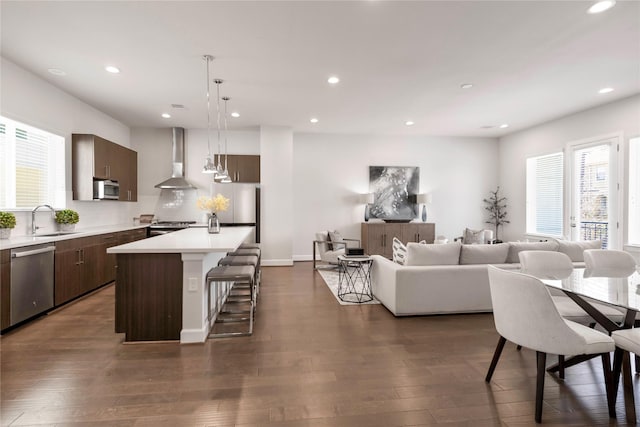 kitchen featuring light countertops, a kitchen bar, appliances with stainless steel finishes, a sink, and wall chimney range hood