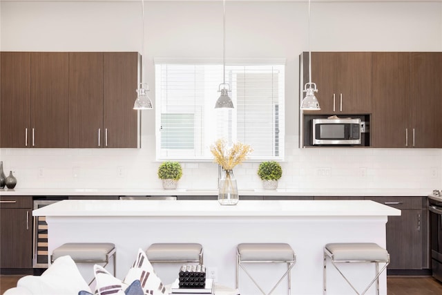 kitchen featuring stainless steel microwave, light countertops, tasteful backsplash, and a breakfast bar