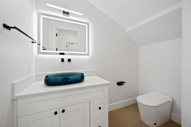 bathroom featuring lofted ceiling, toilet, wood finished floors, vanity, and baseboards