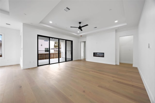 unfurnished living room with recessed lighting, visible vents, light wood-style floors, a raised ceiling, and a glass covered fireplace