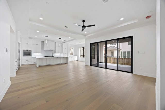 unfurnished living room with a tray ceiling, recessed lighting, visible vents, light wood-style floors, and a ceiling fan