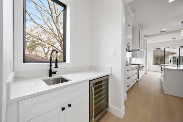 kitchen featuring visible vents, white cabinets, wine cooler, light wood-type flooring, and a sink