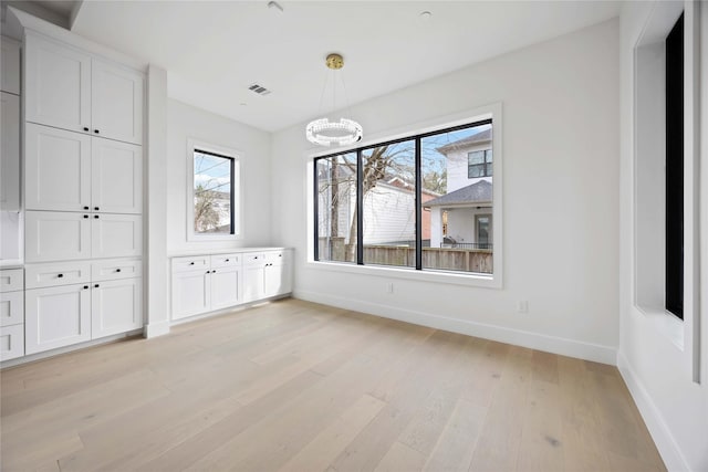 unfurnished dining area with visible vents, light wood-type flooring, an inviting chandelier, and baseboards