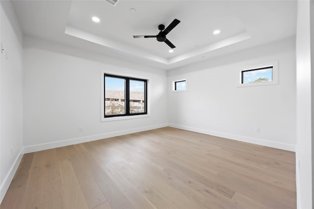 empty room with light wood-type flooring, plenty of natural light, baseboards, and a raised ceiling