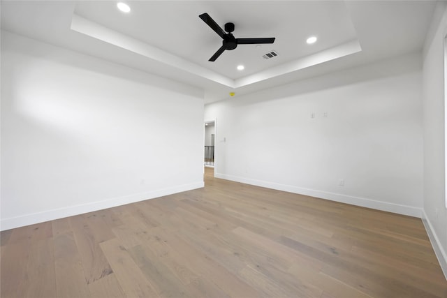 empty room featuring ceiling fan, recessed lighting, wood finished floors, baseboards, and a tray ceiling