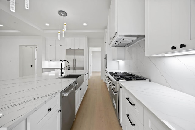 kitchen featuring light stone counters, premium appliances, a sink, white cabinetry, and backsplash