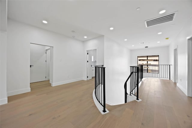 hallway with visible vents, light wood-type flooring, an upstairs landing, and recessed lighting