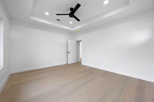 unfurnished room featuring a tray ceiling, light wood finished floors, recessed lighting, visible vents, and baseboards