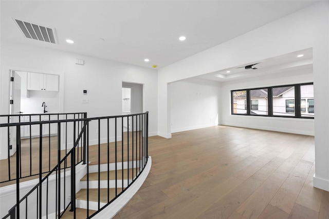 hallway with baseboards, visible vents, wood finished floors, an upstairs landing, and recessed lighting