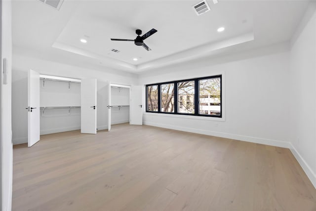 unfurnished bedroom featuring light wood-type flooring, a raised ceiling, visible vents, and baseboards