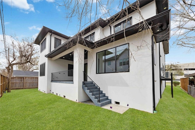 rear view of house featuring a yard, a fenced backyard, a balcony, and stucco siding