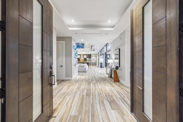 hallway featuring recessed lighting, a raised ceiling, light wood-style flooring, and baseboards