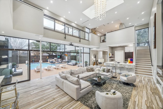 living room with a skylight, light wood finished floors, recessed lighting, a high ceiling, and stairs