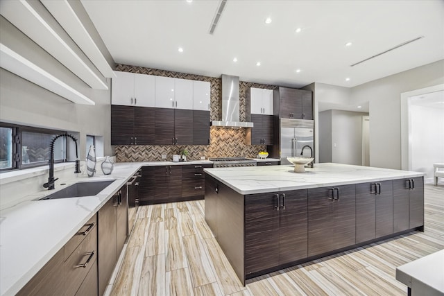 kitchen with stainless steel appliances, backsplash, a sink, modern cabinets, and wall chimney exhaust hood